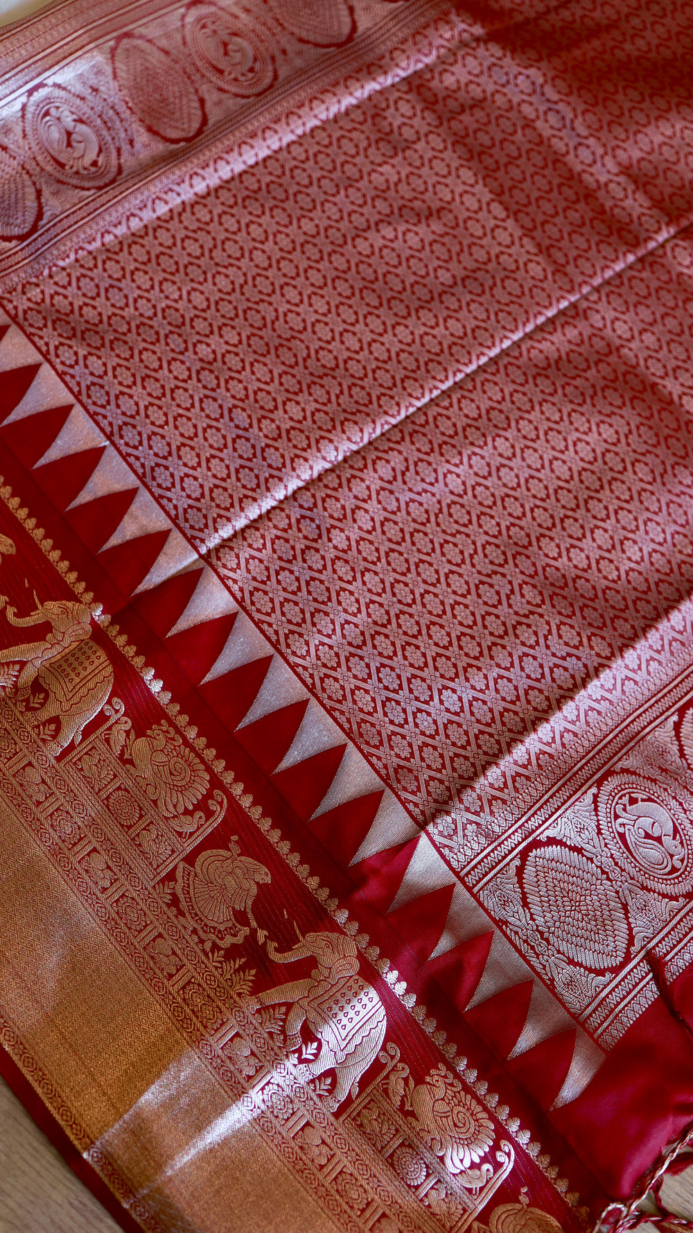 High-angle view of the rich crimson red pallu with intricate silver zari lattice weave and temple triangle border.