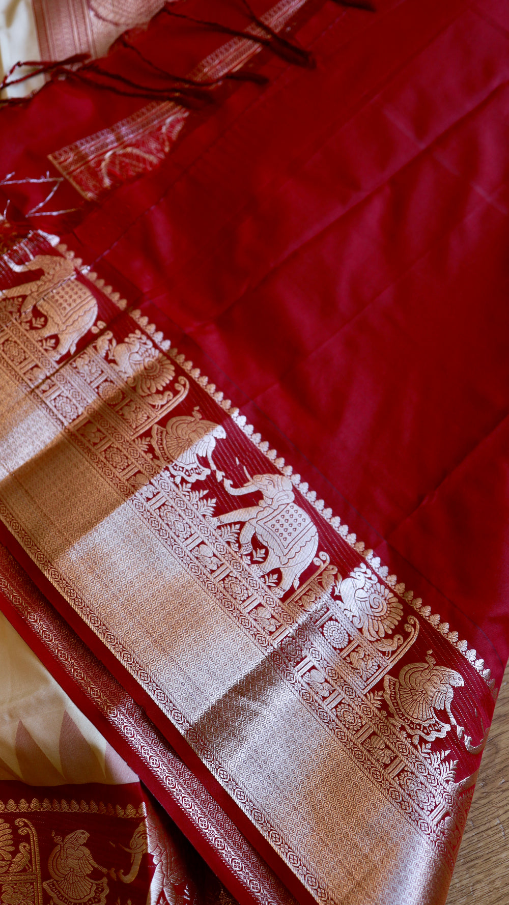 Detail shot of the contrast crimson blouse piece and saree border featuring zari woven elephant and peacock motifs.