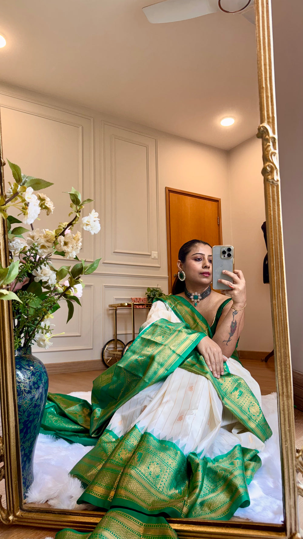 Mirror selfie perspective detailing the drape, gold zari border contrast, and soft silk texture of the off-white and green saree.