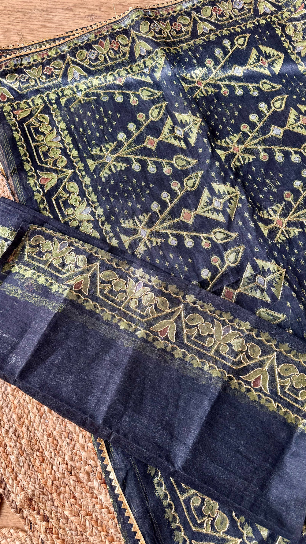 Close-up of Midnight Black Kardana Jamdani Saree showing unstitched blouse piece folded beside detailed floral and geometric pallu border with olive gold threadwork.