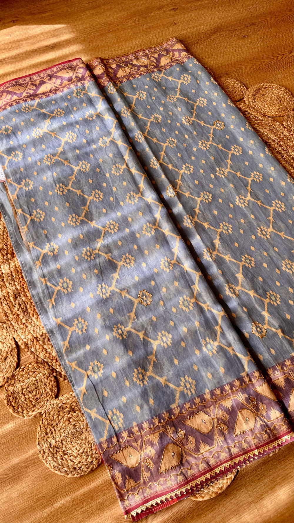 Slate blue Kardana Jamdani saree neatly folded showing geometric body motifs and detailed wine purple embroidered border.