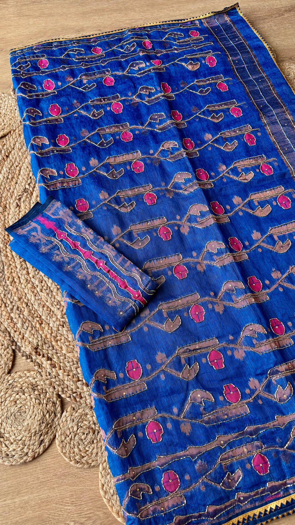 Close-up of Royal Blue Kardana Jamdani Saree pallu showing intricate pink floral hand-embroidery, kardana beadwork vines, and the folded matching blouse piece on a jute mat background.