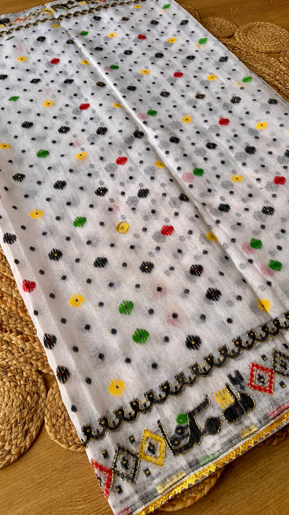 Close-up of off-white Jamdani saree pleats showing scattered colorful polka dots and an embroidered wavy Kardana border.