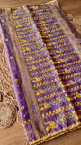 Close-up of handwoven lavender Kardana Jamdani saree pallu featuring mustard yellow motifs, glass beadwork, and mirror embellishments on a woven jute mat background.