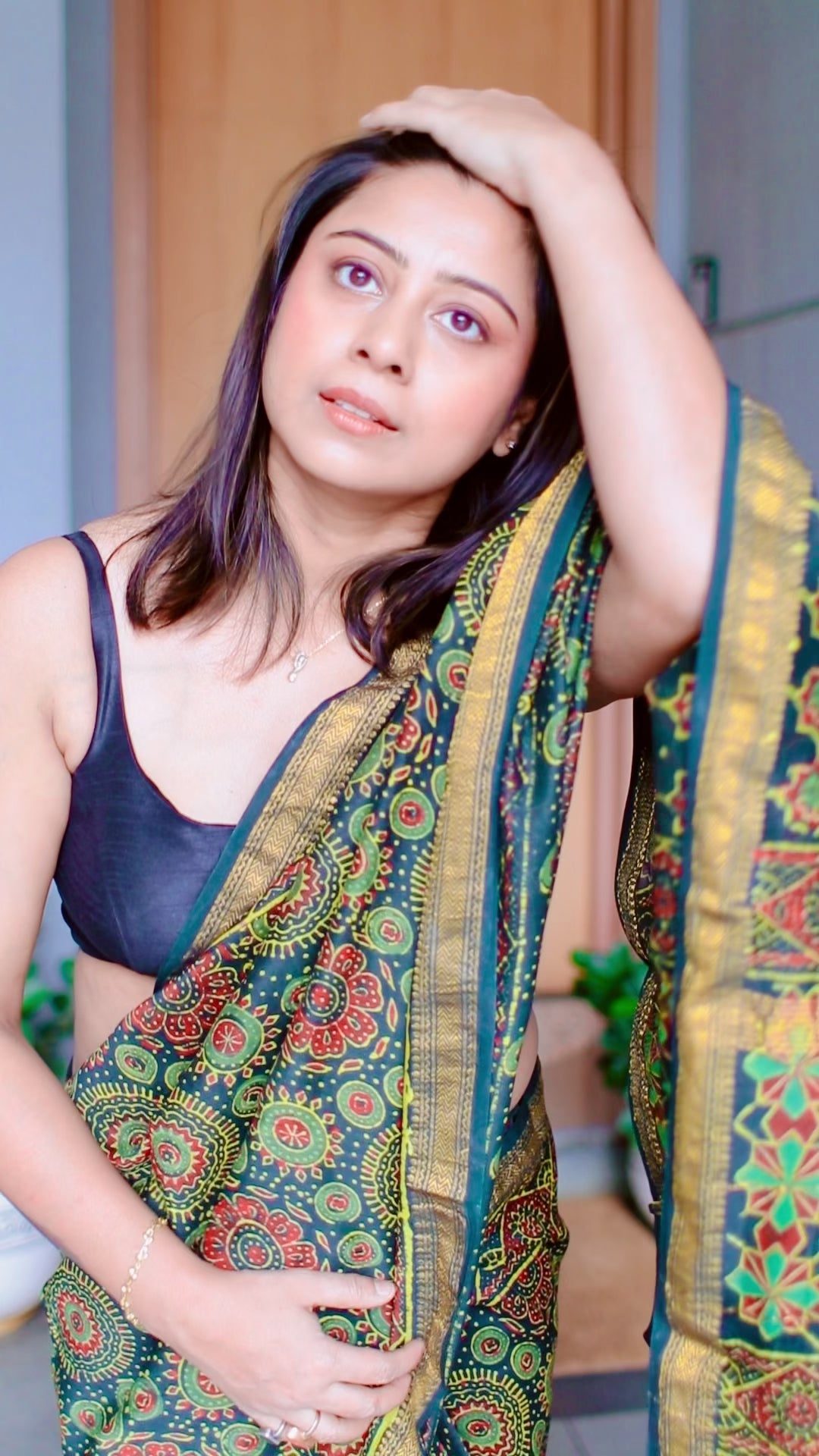 Reel video of Woman draped in a teal Maheshwari Silk Saree with red and green Ajrakh block prints, posing near a wooden door.